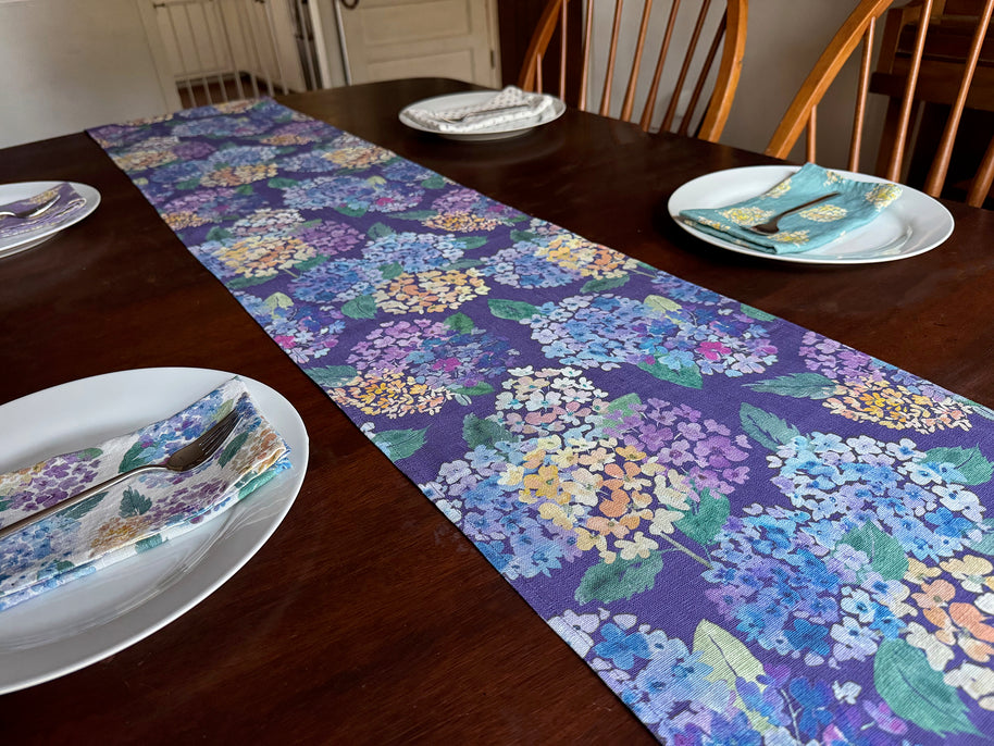 Dining table set with a linen Endless Hydrangea patterned table runner, plates, and linen napkins, all with moss + bloom patterns.