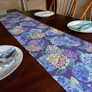 Dining table set with a linen Endless Hydrangea patterned table runner, plates, and linen napkins, all with moss + bloom patterns.