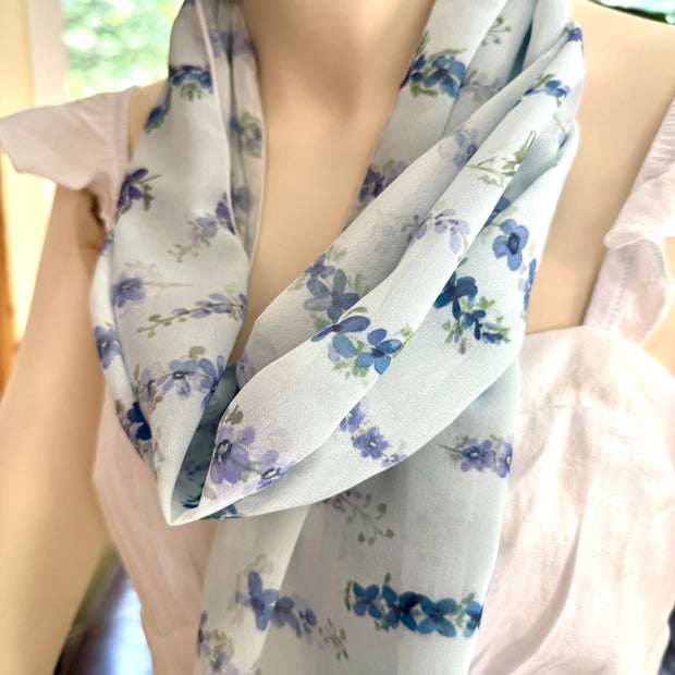 Person wearing a floral scarf with delphinium blue flowers on a blurred background