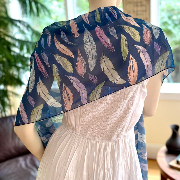 Mannequin wearing a white dress with a blue feather-patterned shawl in a room setting.