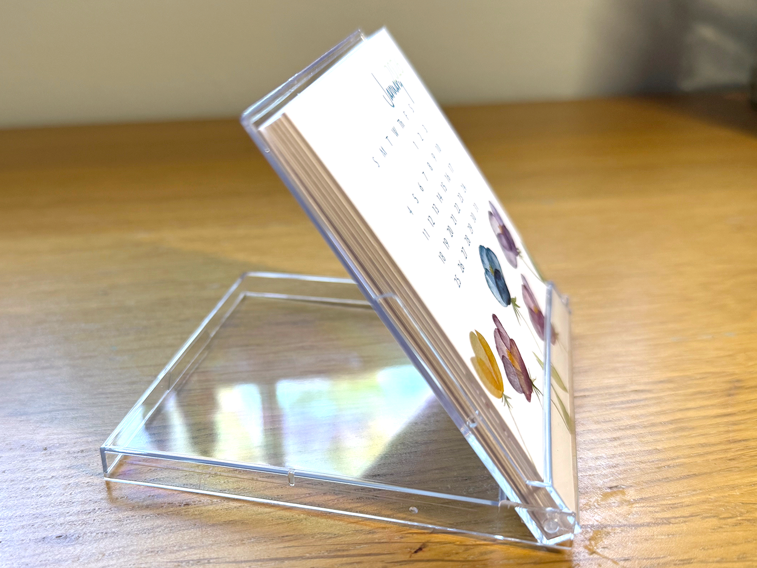 Acrylic stand holding a mini desk calendar on a wooden surface