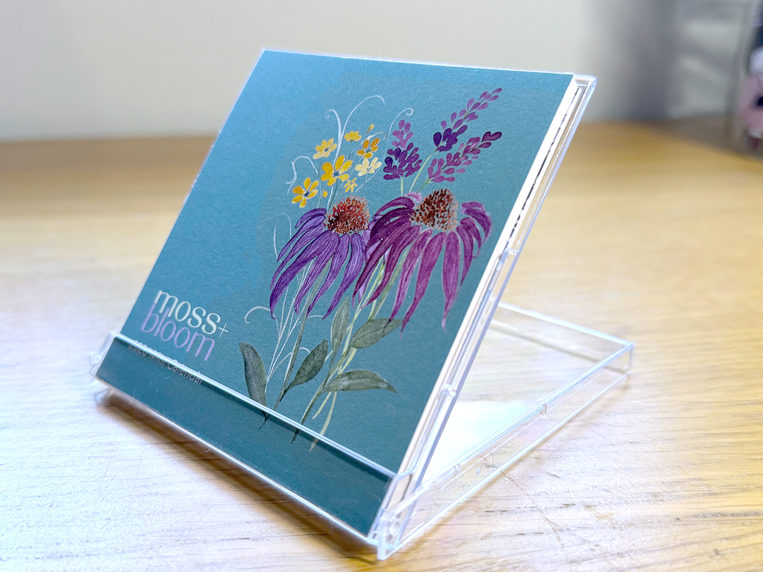 A colorful mini desk calendar with floral design on a stand on a wooden desk