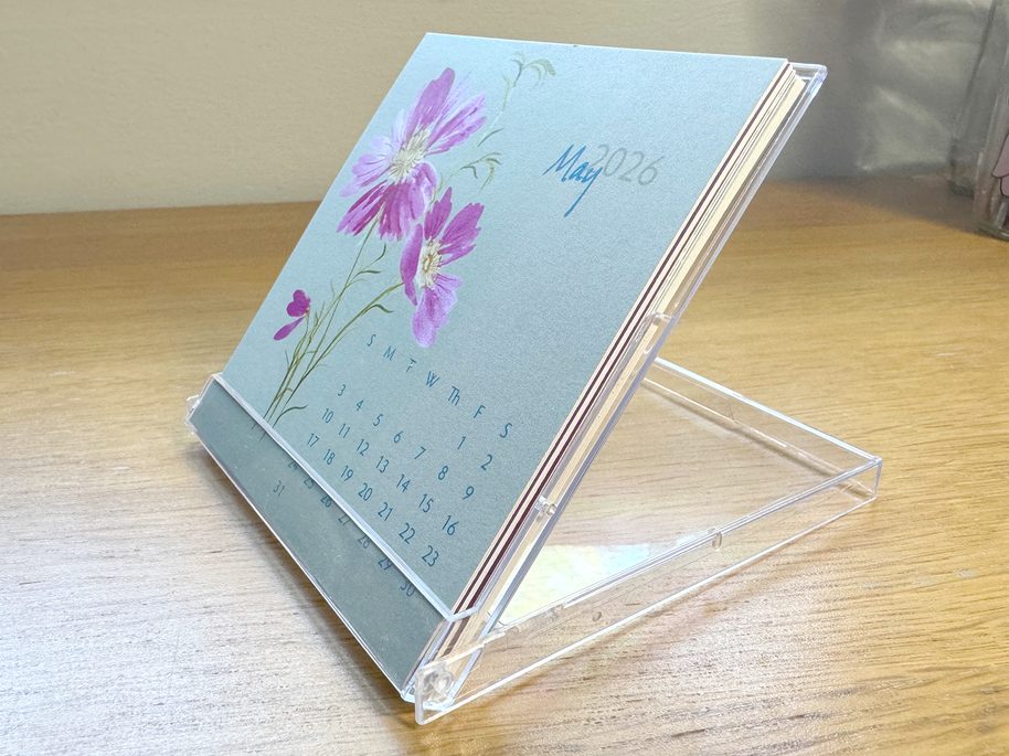 Small calendar with floral design on a stand, placed on a wooden surface.