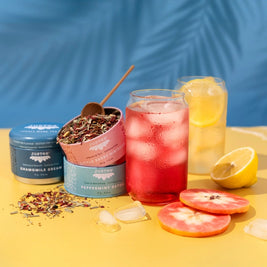 Tea-making setup with loose tea, tea bags, and a iced tea drink on a yellow surface with a blue background.